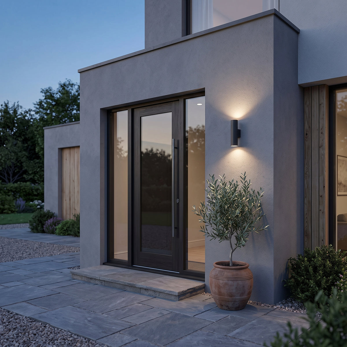 Black Toki up-down cylinder sconce beside a glass front door at dusk