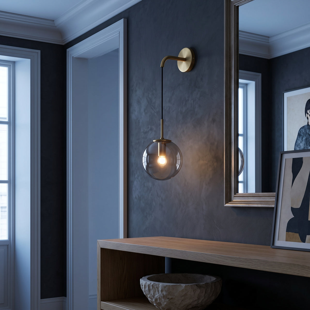 Brass wall sconce with smoky grey glass globe over an oak console