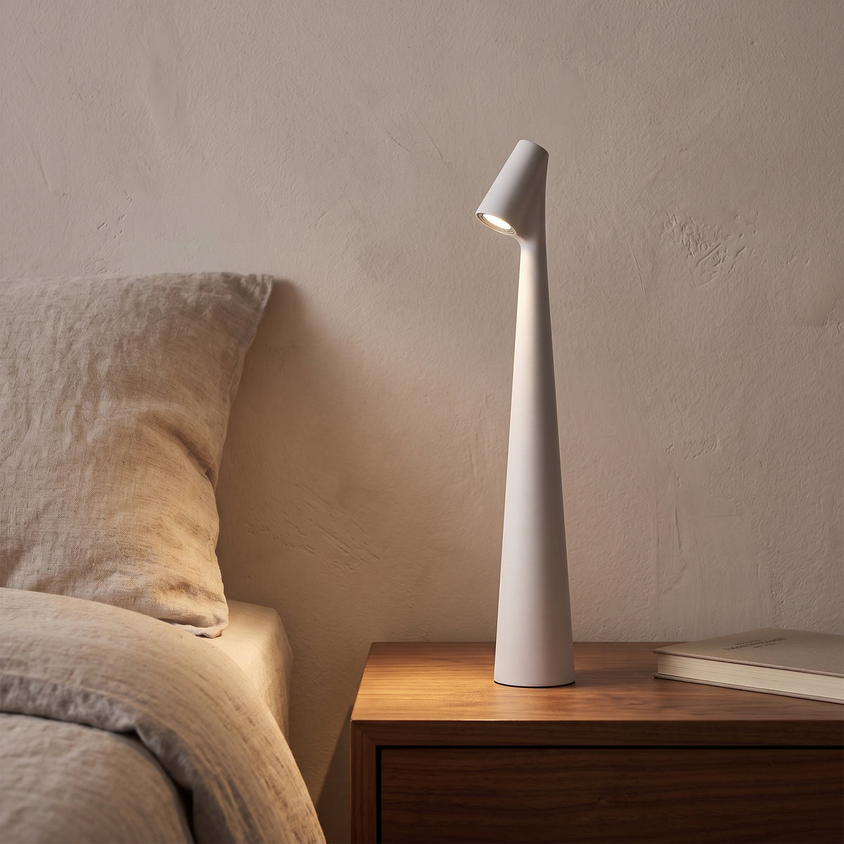 White slim cordless table lamp on a walnut nightstand in the evening