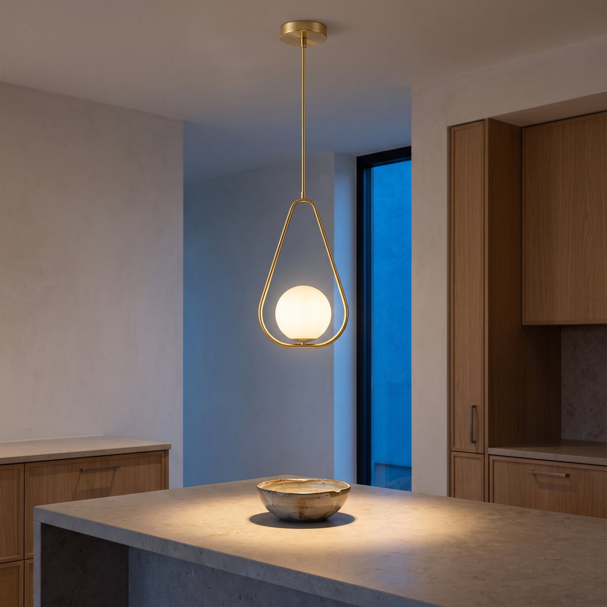 Gold teardrop pendant above a stone kitchen island at blue hour