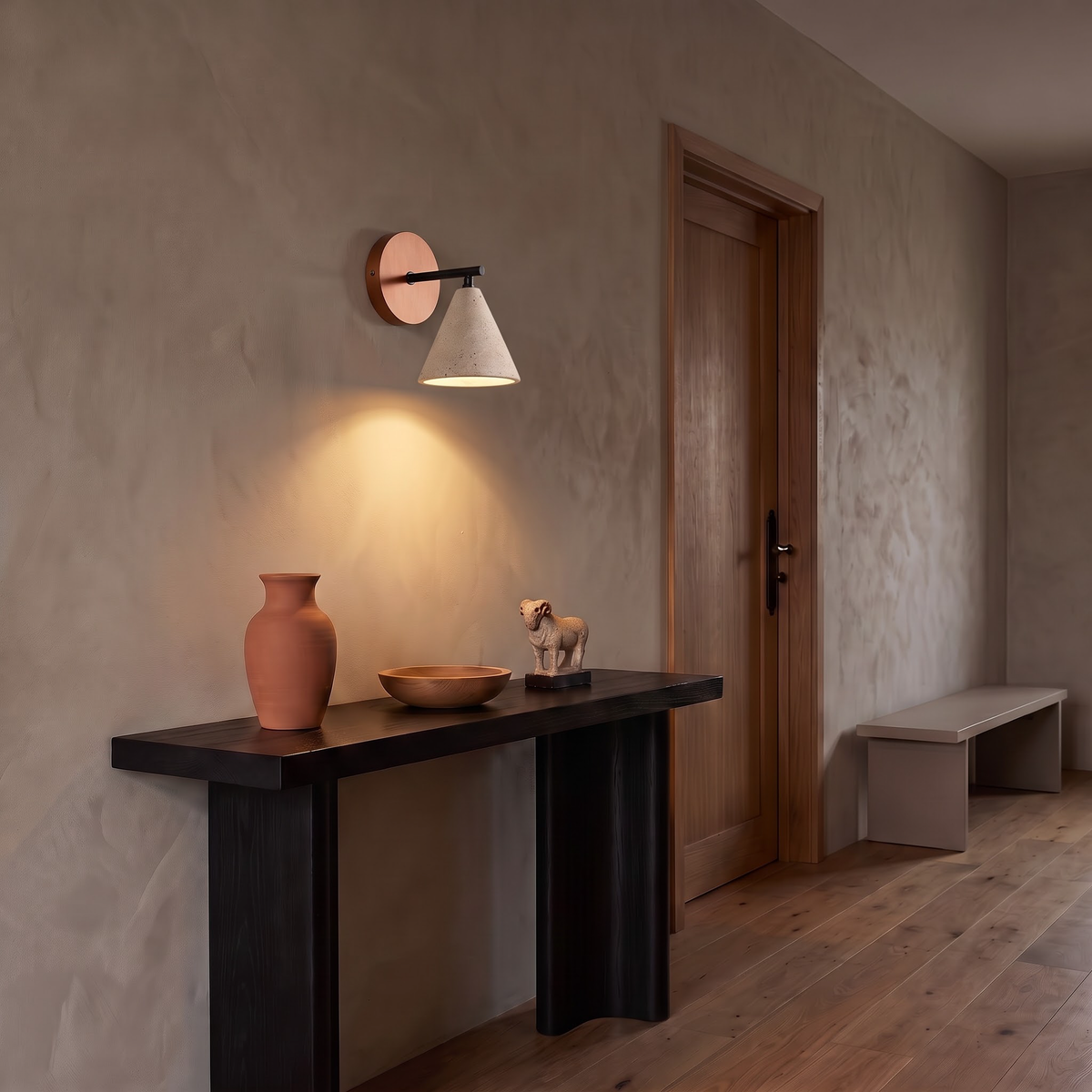 Travertine cone wall light above a dark oak console in an entry