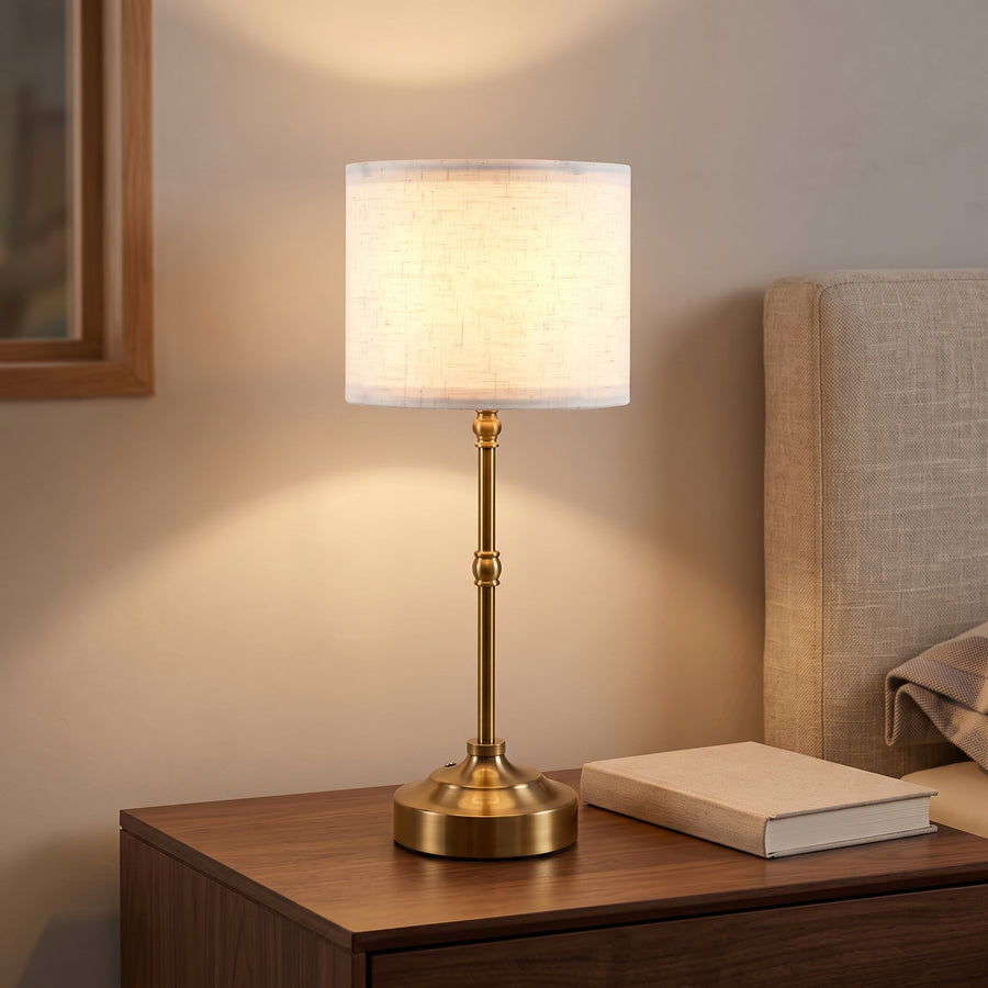 Cordless brass table lamp with white drum shade on a nightstand