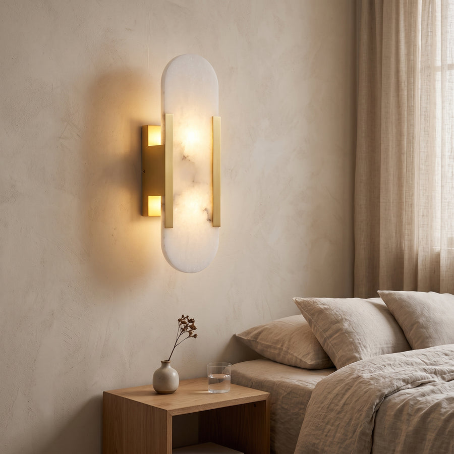 Gold and white marble wall sconce lit beside a bed at dusk