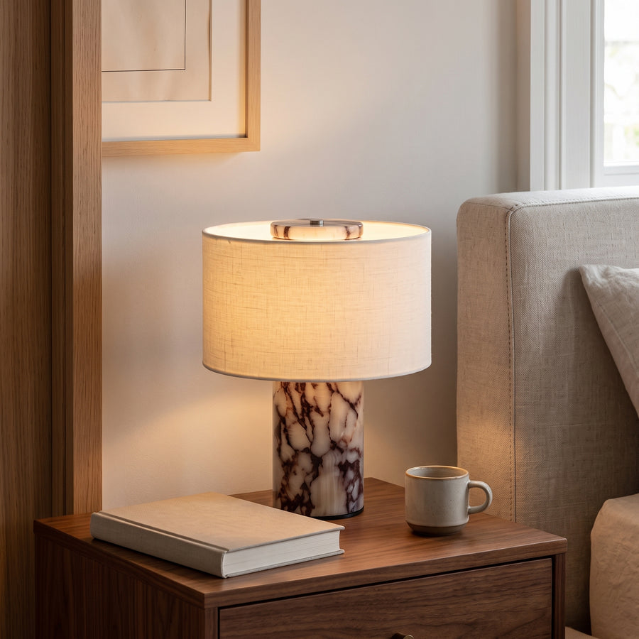 Cordless marble table lamp with linen drum shade glowing on a walnut nightstand